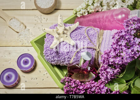 Spa concept with sea salt, perfume, candles, towel and lilac flowers for bath on wooden background. Aromatherapy for relaxation, top view. Stock Photo