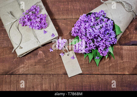 Top view of gift and bouquet of lilacs wrapped in kraft paper on a wooden background. Empty space below. Stock Photo