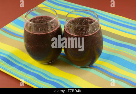 Two cold blueberry smoothie ice drinks in glasses on striped place mat on red table Stock Photo
