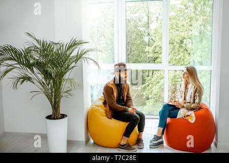 Young man and woman sitting on the comfortable chairs during the psychological counseling, solving some psychological problems in the office Stock Photo