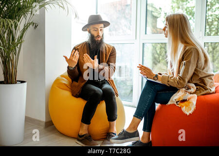 Young man and woman sitting on the comfortable chairs during the psychological counseling, solving some psychological problems in the office Stock Photo