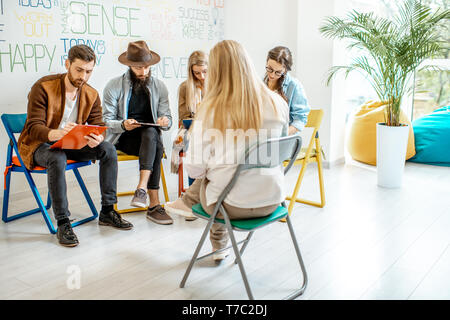 Group of young people sitting together during the psychological therapy with psychologist solving some mental problems in the office Stock Photo