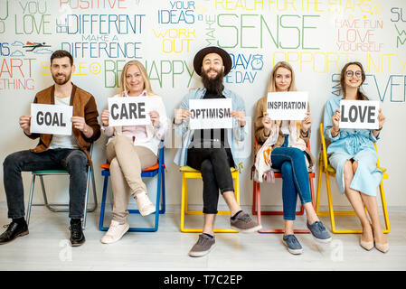 Group of diverse people sitting in a row and holding papers with various inscriptions on the topic of mental health indoors Stock Photo