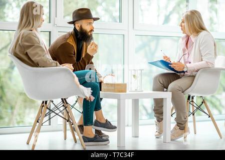 Young couple having misunderstandings during the psychological counseling with senior female psychologist in the office Stock Photo