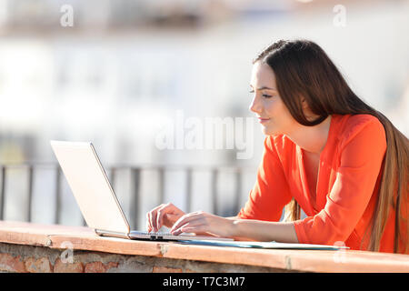 Side view portrait of an entrepreneur entering data on laptop in a balcony Stock Photo