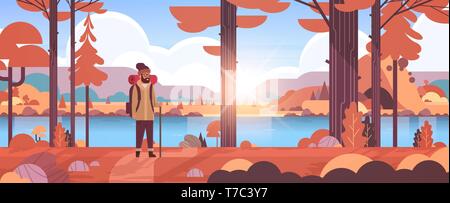 male tourist hiker with backpack man traveler holding stick standing in forest hiking concept sunrise autumn landscape nature river mountains Stock Vector