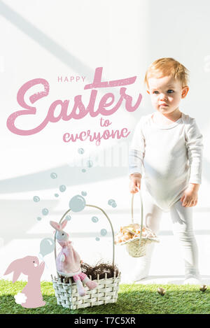 cute babystanding with wicker basket on green grass near golden quail eggs, happy Easter to everyone lettering and rabbit blowing soap bubbles illustr Stock Photo