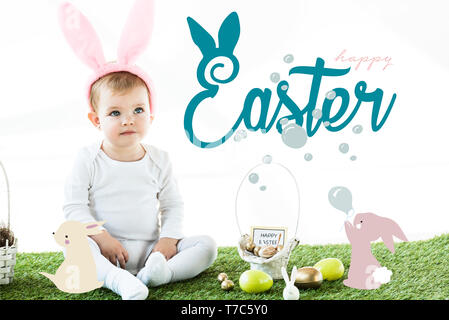 cute baby in bunny ears headband sitting near painted chicken and quail eggs and Easter illustration Stock Photo