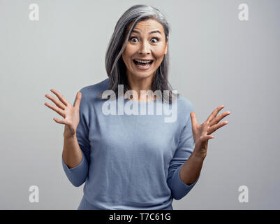 Beautiful Middle-Aged Asian Woman Shows Emotions of Excitement and Happyness in Studio. Her Face is in Happy Surprise and Hands Raised Up. Tonned Port Stock Photo