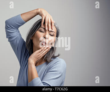 Beautiful Grey-Haired Female Model Posing For The Camera. Charming Middle-Aged Asian Woman Touching Her Face With Hands While Posing At The Photo Stud Stock Photo