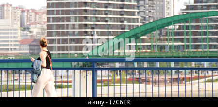 Belgrade, Serbia - April 26, 2019: Young woman walking over the city bridge with the view on Belgrade Waterfront project Stock Photo