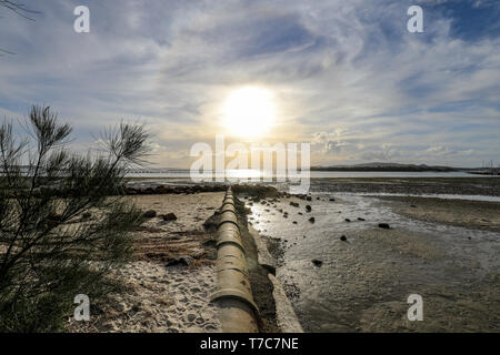 Stormwater pipe leading to sun setting over ocean Stock Photo