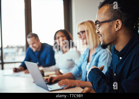 Smiling young African American businessman discussing work while sitting with a diverse group of colleagues during a meeting Stock Photo