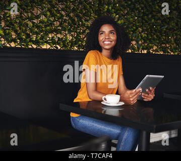 Happy young woman sitting in cafe holding digital tablet Stock Photo