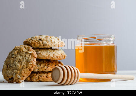 Golden liquid polyfloral spring honey inside a glass jar next to a stack of oatmeal cookies with nuts and sesames. Healthy Vegan Breakfast. Stock Photo