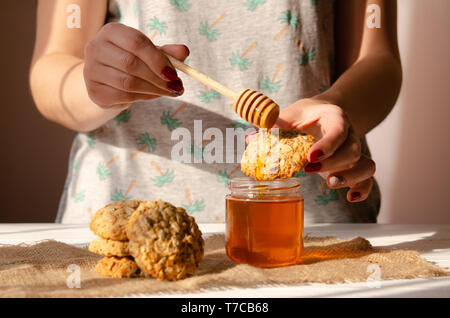 The yong woman drips golden liquid honey on oatmeal with nuts and sesame cookies. Stock Photo