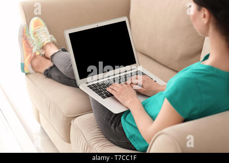 Young female freelancer working with laptop on sofa at home Stock Photo