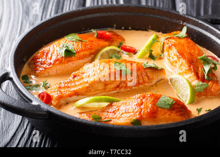 Fillet salmon in spicy Thai coconut sauce with lime and herbs close-up in a pan on the table. horizontal Stock Photo