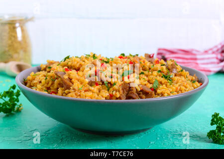 Bulgur with chicken and vegetables. Delicious healthy warm salad on a bright background. Bulgur pilaf Stock Photo