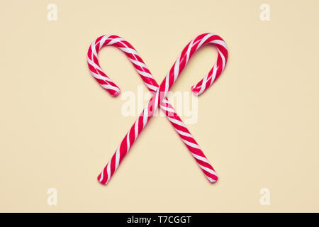 Shiny red and white traditional candy canes crossed on beige background Stock Photo