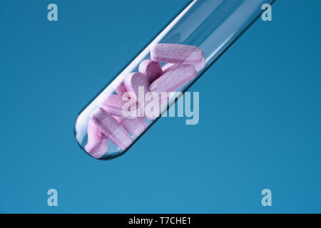 Laboratory glass test tube filled with pink pills on blue backround. Medicine research concept. Stock Photo