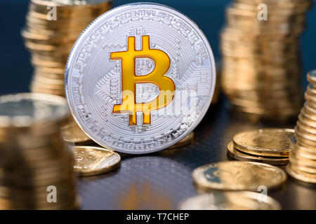 Bitcoin. Silver bitcoin coin between golden coins stacks with reflection. Stock Photo
