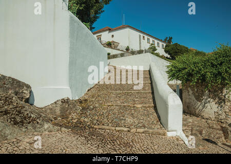 Whitewashed wall and pathway made of rough stone with large stairs going up the hill at Marvao. A medieval hamlet perched on a crag in Portugal. Stock Photo