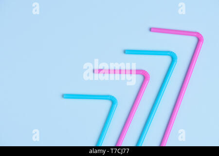 Pink and blue pastel colored drinking cocktail straws on blue paper background with side copy space Stock Photo