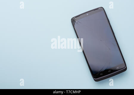 Smartphone with broken glass screen phone touch screen on blue background with copy space. Stock Photo
