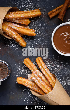Churros with sugar powder chocolate sauce dip and cinnamon sticks on dark background flat lay top view Stock Photo