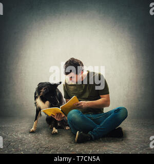 Curious purebred border collie dog and his master reading together an interesting book. Owner seated on floor training his cute puppy isolated over gr Stock Photo