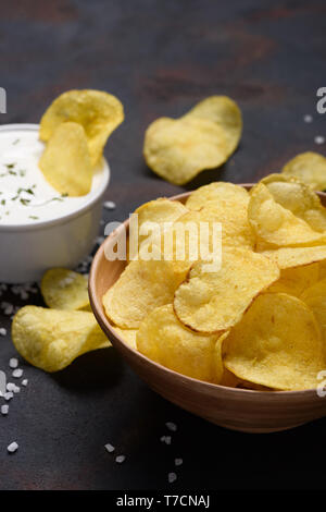Crispy potato chips in bowl with sauce dip and salt on dark table Stock Photo
