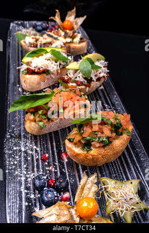 Tasty savory tomato Italian appetizers, or bruschetta, on slices of toasted baguette garnished with basil and avocado. Stock Photo