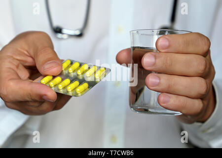 Doctor holding pills and glass of water, therapist giving medication in blister pack with yellow capsules. Concept of medical prescription, drugs Stock Photo