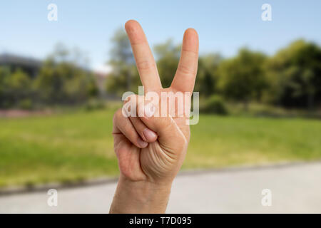 Closeup of man making peace or victory gesture with index and middle finger having green nature background Stock Photo