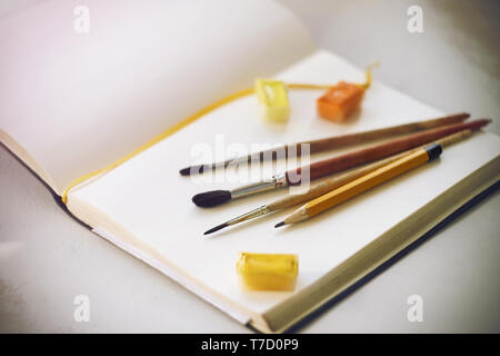 On the album there are art supplies prepared for drawing: brushes from squirrel pile, pencil and watercolor paints. Stock Photo