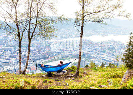 Two women on top of Mount Fløyen relaxing in a hammock looking over a scenic view of Bergen, Norway Stock Photo