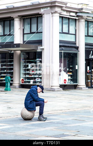 Sad lonely man sitting on a ball in a city Stock Photo