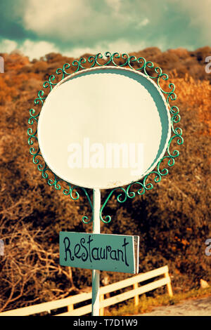 White blank oval metal sign and a wooden rectangular restaurant signboard with forest and sky background Stock Photo