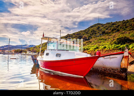 Red and white painted old boats washed upon the shore at Gumusluk bay in Bodrum, Turkey. Stock Photo