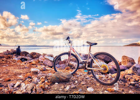 Old rusty bicycle parked on the seashore and an angler fisherman fishing near the sea