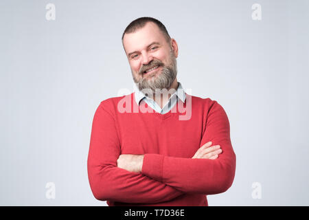 Mature man with beard holding hands crossed and looking at camera while smiling Stock Photo