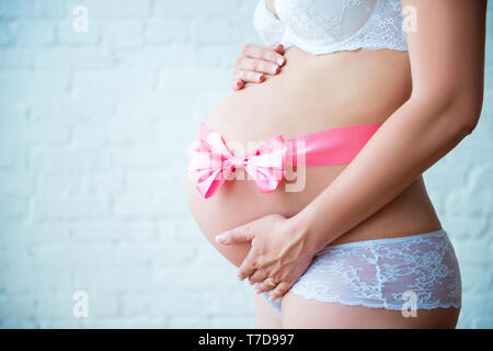 Side view close-up of pregnant woman belly with pink ribbon bow. Waiting for a daughter. Healthy pregnancy and happy maternity. Stock Photo