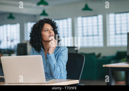 Young businesswoman thinking while using a laptop at work Stock Photo