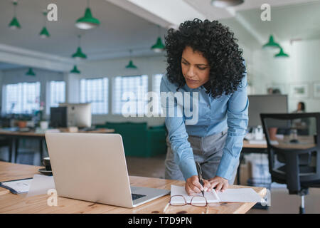 Focused young businesswoman standing at her office desk writing notes Stock Photo