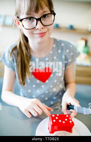 Young girl with red heart on t-shirt and knife in hand going to slice red cake with white dots. Stock Photo