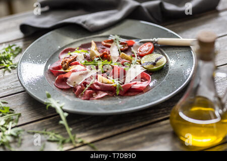 Beef carpaccio on plate with dried tomatoes artichokes arugula and parmesan cheese Stock Photo