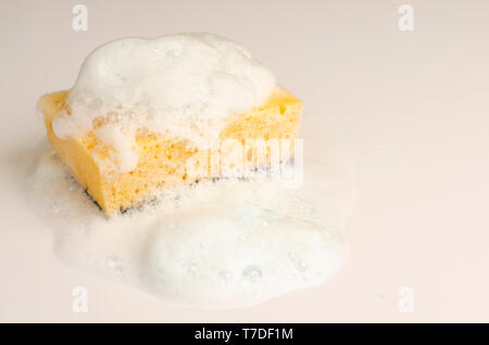 Yellow soapy sponge with foam on white background. Copy space. Stock Photo