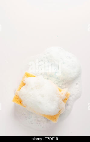 Yellow soapy sponge with foam on white background. Copy space. Stock Photo