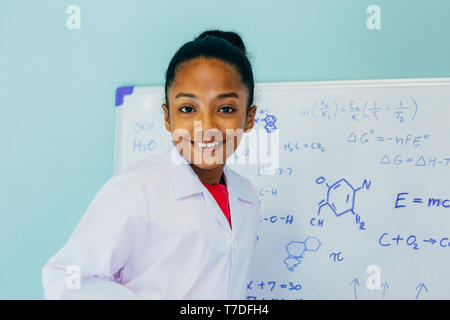 African American girl in lab coat drawing mathematic and science formulas on white board. Creativity and Education concept Stock Photo